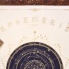 Upper half of the Ephemeris 2027 print showing gold lettering, lunar phases and a navy-blue celestial chart.
